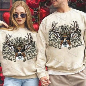 Puede incluir: Sudaderas beige con un gr&aacute;fico de ciervo con gafas de sol y un sombrero de camuflaje. El gr&aacute;fico est&aacute; dentro de un hex&aacute;gono con el texto "100 DAYS OF SCHOOL". Llevadas por un hombre y una mujer.