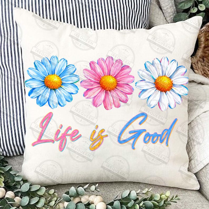 Pu&ograve; includere: Un cuscino quadrato bianco sporco con tre grandi fiori di margherita blu, rosa e bianchi con centri gialli. La frase "Life is Good" &egrave; scritta in una sceneggiatura colorata in basso.
