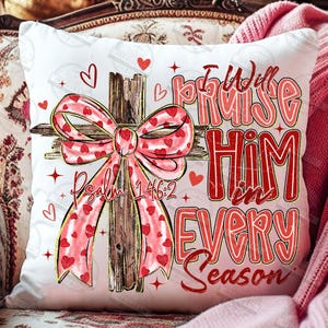 May include: White square pillow with a cross design. The cross is made of wood and has a pink bow with red hearts. The text "I Will Praise Him in Every Season" and "Psalm 146:2" are in red.