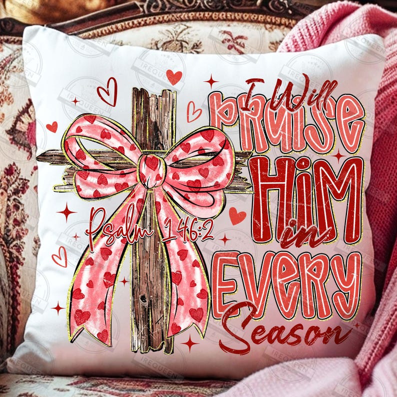 May include: White square pillow with a cross design. The cross is made of wood and has a pink bow with red hearts. The text "I Will Praise Him in Every Season" and "Psalm 146:2" are in red.