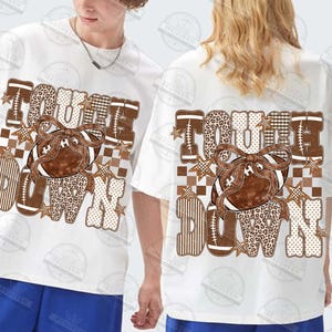 Peut inclure: Un t-shirt blanc &agrave; manches courtes orn&eacute; d'un ballon de football am&eacute;ricain marron avec un n&oelig;ud, entour&eacute; du texte TOUCH DOWN en lettres capitales. Le motif int&egrave;gre des imprim&eacute;s l&eacute;opard, &agrave; carreaux et ray&eacute;s avec de petites &eacute;toiles.