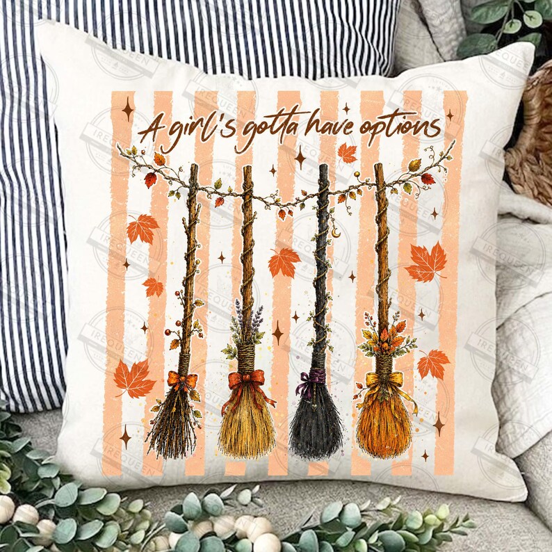 May include: A square throw pillow with a cream background and vertical orange stripes. The design features four decorative brooms hanging from a vine with autumn leaves and the text A girl's gotta have options in brown cursive script.