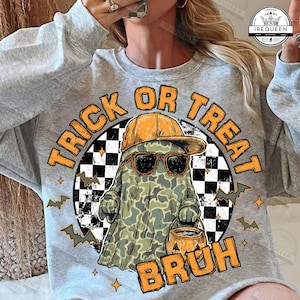 May include: A light gray sweatshirt with a Halloween-themed graphic. The graphic features a ghost wearing sunglasses and a hat, holding a pumpkin bucket, with the words "Trick or Treat Bruh". Bats and stars surround the central image.