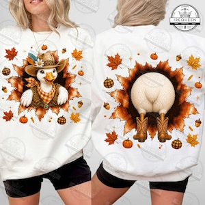 May include: A white sweatshirt featuring a graphic of a duck wearing a cowboy hat and bandana on the front, and the back view of the duck wearing cowboy boots on the back. The design is surrounded by orange and brown autumn leaves, acorns, and pumpkins.