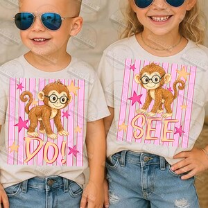 Puede incluir: Dos camisetas infantiles con un mono de dibujos animados con gafas. El mono est&aacute; sobre un fondo de rayas rosas con estrellas y la palabra "DO!" en una camiseta y "SEE" en la otra. Las camisetas son beige.