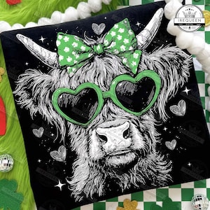 May include: Black t-shirt featuring a Highland cow illustration. The cow wears green heart-shaped sunglasses and a green bow with white shamrocks. The design includes white hearts and stars on a black background.