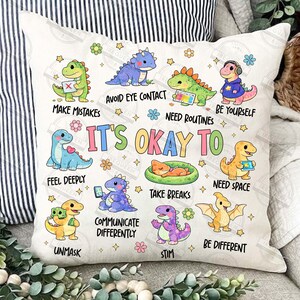 May include: A square cushion with a dinosaur design in various colours. The cushion features cartoon dinosaurs with phrases such as "It's Okay To Feel Deeply" and "Be Yourself". The design includes flowers and stars.