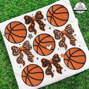 May include: A white fabric with basketball and bow designs. The basketballs are orange with black lines, and the bows have basketball or leopard print patterns. Small star shapes are scattered around the designs.