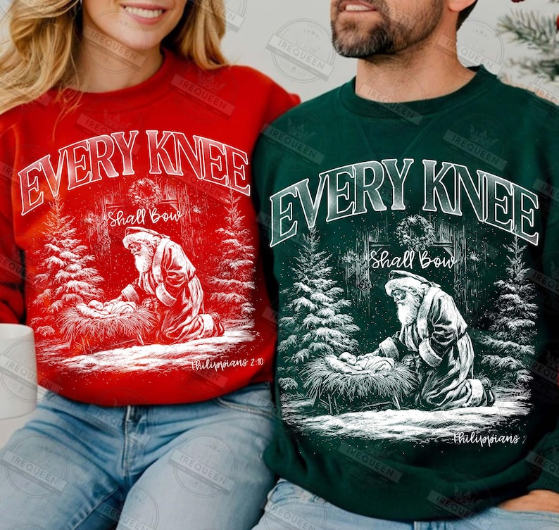 May include: Red and green Christmas sweatshirts with the text "EVERY KNEE Shall Bow" in white. Each sweatshirt features a graphic of Santa kneeling before a manger scene, surrounded by pine trees. The text "Philippians 2:10" is also visible.
