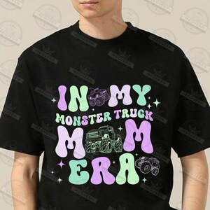 May include: Black t-shirt with a graphic design that says "In My Monster Truck Mom Era" in a retro font. The graphic features a monster truck and stars.
