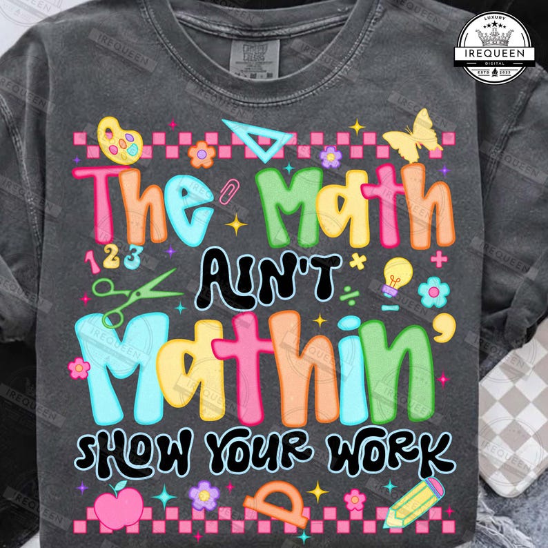 Puede incluir: Camiseta gris oscuro con un gr&aacute;fico colorido que dice "The Math Ain't Mathin' Show Your Work". El dise&ntilde;o incluye s&iacute;mbolos matem&aacute;ticos, una mariposa, flores y un l&aacute;piz. La camiseta es de cuello redondo.