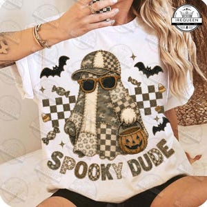 May include: A white t-shirt featuring a graphic of a ghost wearing a baseball cap and sunglasses, holding a jack-o'-lantern bucket. The design includes black bats, checkered patterns, and the text SPOOKY DUDE in a textured, camo-patterned font.