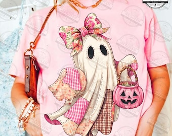 May include: A pink t-shirt featuring a whimsical ghost design. The ghost wears a floral bow and holds a pink pumpkin basket. The ghost's patchwork design includes pink and brown fabrics, perfect for Halloween.