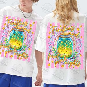 May include: White t-shirts with a colorful graphic design. The design features a mason jar filled with fireflies, surrounded by a pink and yellow floral pattern, and the text "Fireflies and front porch nights."