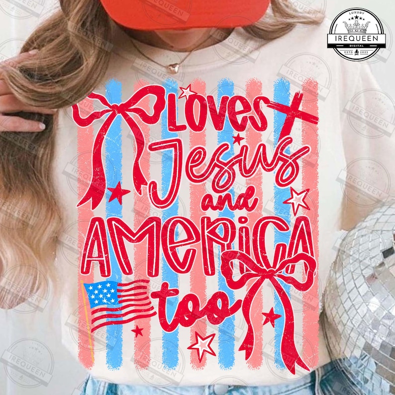 Puede incluir: Camiseta color crema con un dise&ntilde;o patri&oacute;tico. El gr&aacute;fico presenta rayas rojas y azules, estrellas y el texto "Loves Jesus and America too" en una fuente de escritura. Tambi&eacute;n se incluye una bandera estadounidense.