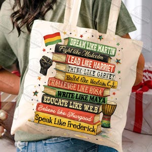 May include: Cream-colored tote bag featuring a stack of books with inspirational phrases like "Dream Like Martin" and "Fight like Malcolm." A black fist and a flag are also depicted. A small drum is visible.