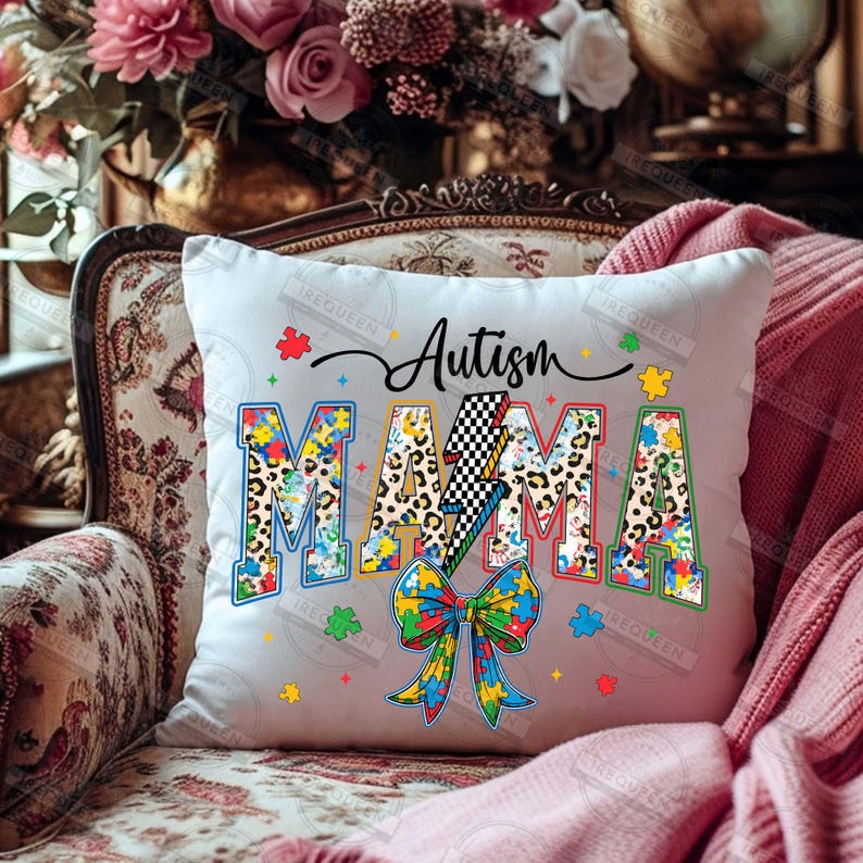 May include: White throw pillow with the text "Autism Mama" in colorful letters with a lightning bolt and puzzle pieces. The letters are decorated with a leopard print pattern.