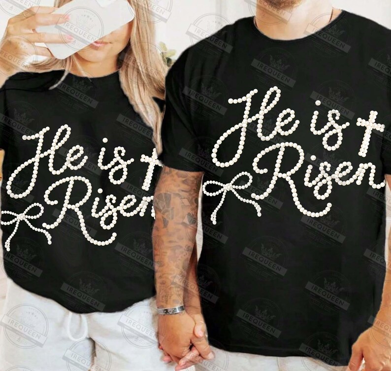 May include: Black t-shirts with the text "He is Risen" in a white, cursive font. The design includes a cross and a bow. The shirts are likely for Easter or religious events.