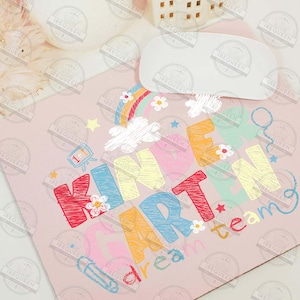 May include: A pink mousepad with the words "KINDERGARTEN ART team" in colorful, sketched letters. A rainbow, clouds, stars, and flowers decorate the design. A pencil and the word "dream" are also included.