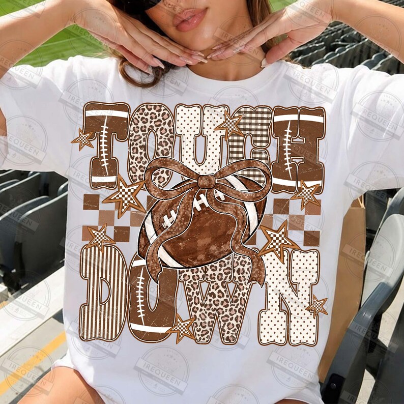Peut inclure: Un t-shirt blanc avec un motif graphique marron portant le texte TOUCH DOWN. Le design comprend un ballon de football, un grand n&oelig;ud, des &eacute;toiles et divers motifs comme l'imprim&eacute; l&eacute;opard, le carreau et les rayures en tons marron, beige et blanc.