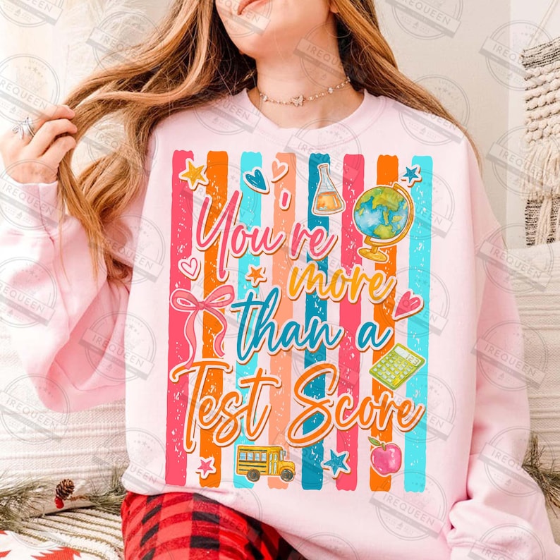 Może przedstawiać: Jasnor&oacute;żowa bluza z kolorowymi pionowymi paskami i napisem "You're more than a Test Score". Projekt zawiera globus, szkolny autobus, jabłko i inne grafiki związane ze szkołą.