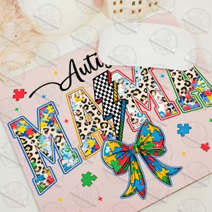 May include: A pink background with the words "Autism Mama" in colorful letters with a leopard print and puzzle piece pattern. A large blue, yellow, green, and red puzzle piece bow is in the center of the design.