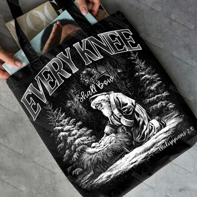 May include: Black tote bag featuring a black and white illustration of Santa kneeling before baby Jesus. The text "EVERY KNEE Shall Bow" is displayed above the image, with "Philippians 2:10" below.