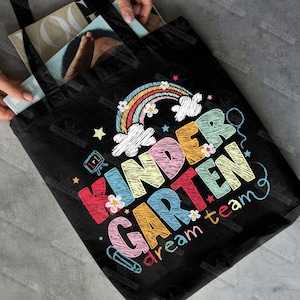 May include: Black tote bag with a colorful "Kindergarten dream team" design. The design includes a rainbow, stars, flowers, and a pencil. The text is in various colors, with a chalkboard style.