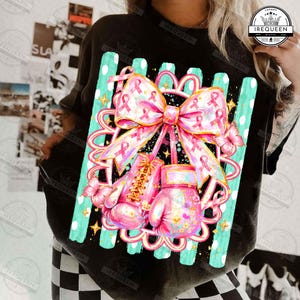 May include: A black t-shirt featuring a graphic print of two pink boxing gloves tied together with a large pink ribbon decorated with breast cancer awareness symbols, surrounded by pink butterflies and teal vertical stripes with white dots.