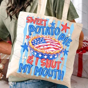 May include: A beige tote bag with a patriotic design. The bag features the text "Sweet Potato Pie & I Shut My Mouth" in blue and red, along with a pie graphic resembling the American flag. Blue and red stars decorate the design.