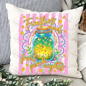May include: White square pillow with a colorful design featuring a mason jar filled with fireflies. The jar is surrounded by flowers and the words "Fireflies and front porch nights" in yellow script. Pink stripes and stars frame the design.