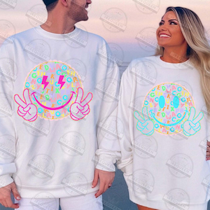 May include: White sweatshirts featuring a colorful smiley face design. The design includes a smiley face with peace signs, lightning bolts, and letters. The sweatshirts are long-sleeved and suitable for casual wear.