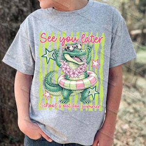 May include: A gray t-shirt featuring a cartoon alligator wearing sunglasses, a flower lei, and a swim ring. The text "See you later" and "School's out for summer" are displayed in pink and green.
