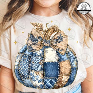 May include: A white t-shirt featuring a patchwork pumpkin design. The pumpkin is composed of various blue and beige patterned fabrics, with a large bow and stem. Gold stars and the text "IREQUEEN" are also visible.