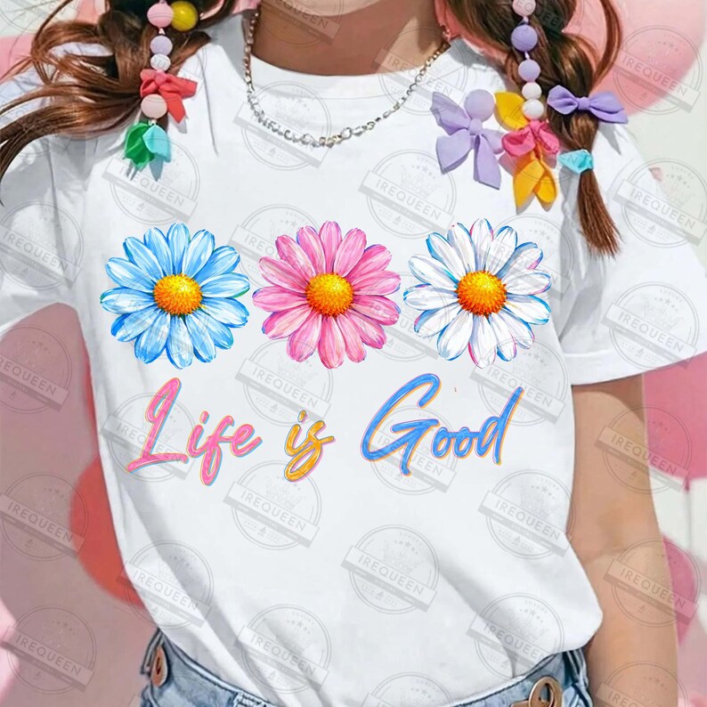 Pu&ograve; includere: T-shirt bianca con tre fiori di margherita colorati in blu, rosa e bianco con centri gialli. La frase "Life is Good" &egrave; scritta in un carattere giocoso sulla parte anteriore.