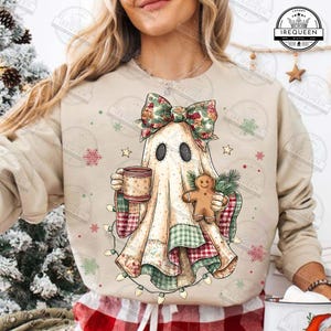 以下が含まれることがあります： ベージュのスウェットシャツに、気まぐれなゴーストのデザイン。ゴーストは花の弓を身につけ、マグカップとジンジャーブレッドマンを持ち、パッチワーク生地で覆われています。お祝いのライトと雪片がホリデーテーマに加わります。