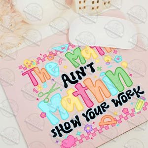 Puede incluir: Una alfombrilla de rat&oacute;n rosa con el texto "The math ain't mathin' show your work" en letras coloridas. El dise&ntilde;o incluye gr&aacute;ficos escolares como tijeras, un transportador y un l&aacute;piz.