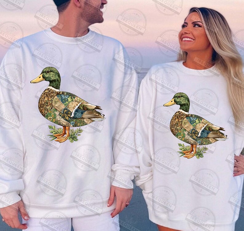 May include: White sweatshirts featuring a detailed duck illustration. The duck has a green head, yellow beak, and a body with a patterned design. The sweatshirts are long-sleeved and suitable for casual wear.