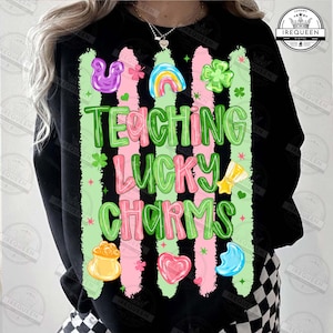 Puede incluir: Sudadera negra con el texto "TEACHING LUCKY CHARMS" en verde y rosa. El diseño incluye un arcoíris, tréboles, un pote de oro y otros amuletos de la suerte. La sudadera tiene cuello redondo y mangas largas.