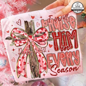 May include: A light pink t-shirt featuring a wooden cross with a red and pink heart-patterned bow. The text "I will praise Him in every season" and "Psalm 146:2" are printed in red.