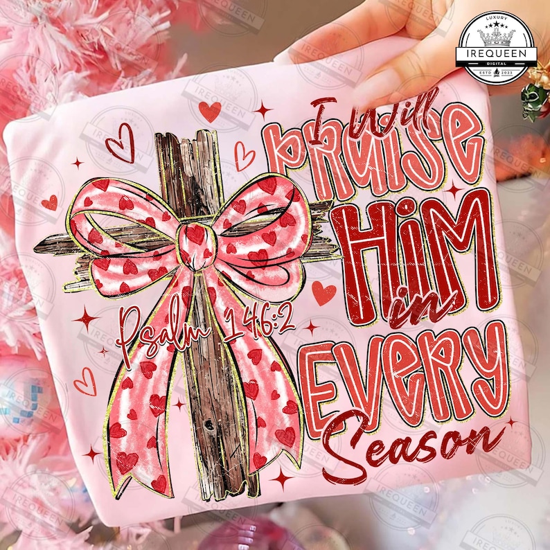 May include: A light pink t-shirt featuring a wooden cross with a red and pink heart-patterned bow. The text "I will praise Him in every season" and "Psalm 146:2" are printed in red.