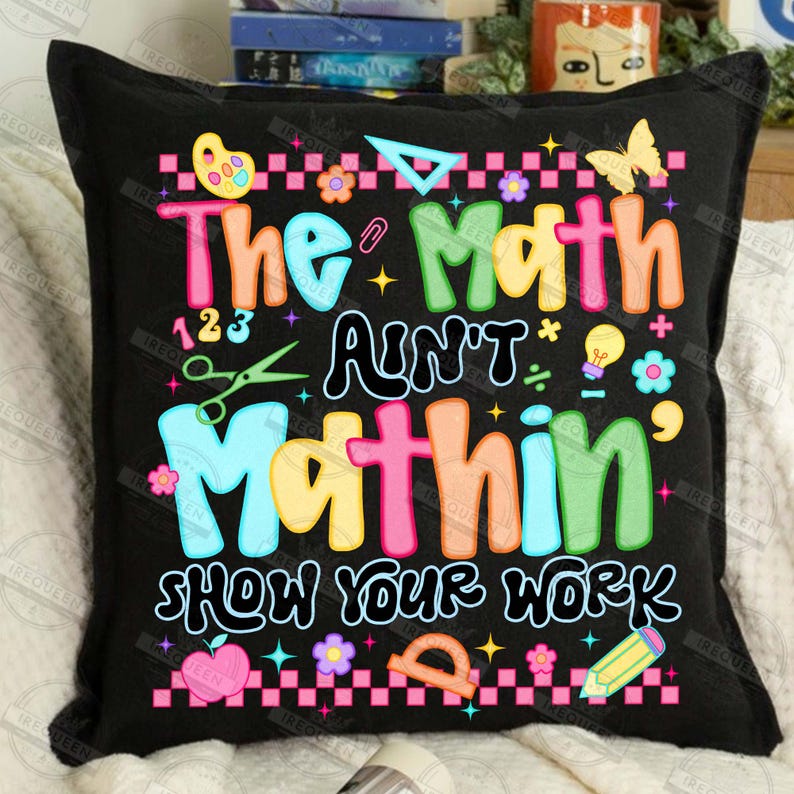 Puede incluir: Coj&iacute;n cuadrado negro con el texto "The Math Ain't Mathin' Show Your Work" en letras coloridas. El dise&ntilde;o incluye s&iacute;mbolos matem&aacute;ticos, una mariposa, flores y un l&aacute;piz.