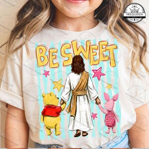 Könnte beinhalten: Cremefarbenes T-Shirt mit den Worten "BE SWEET" in Gelb und Blau. Die Grafik zeigt eine Illustration von Jesus mit Winnie Puuh und Ferkel. Rosa und gelbe Sterne sind verstreut.