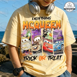 May include: A light yellow t-shirt featuring a graphic print of Lightning McQueen and other characters from the Cars franchise dressed in Halloween costumes, with the text LIGHTNING MCQUEEN and TRICK OR TREAT printed in black and orange.