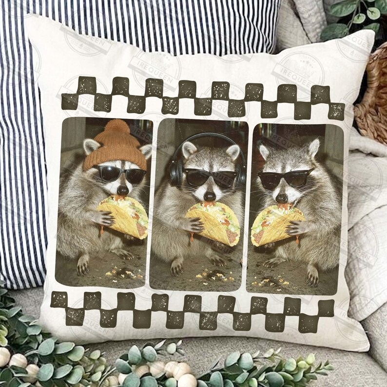 May include: A cushion with a print of three raccoons, each wearing sunglasses and eating a taco. One raccoon wears a beanie, another headphones. The cushion has a checkered border and is on a white background.
