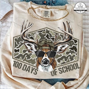 Puede incluir: Una sudadera beige con un gr&aacute;fico de un ciervo con gafas de sol y una gorra de camuflaje. El gr&aacute;fico est&aacute; sobre un fondo de camuflaje e incluye el texto "100 Days of School."
