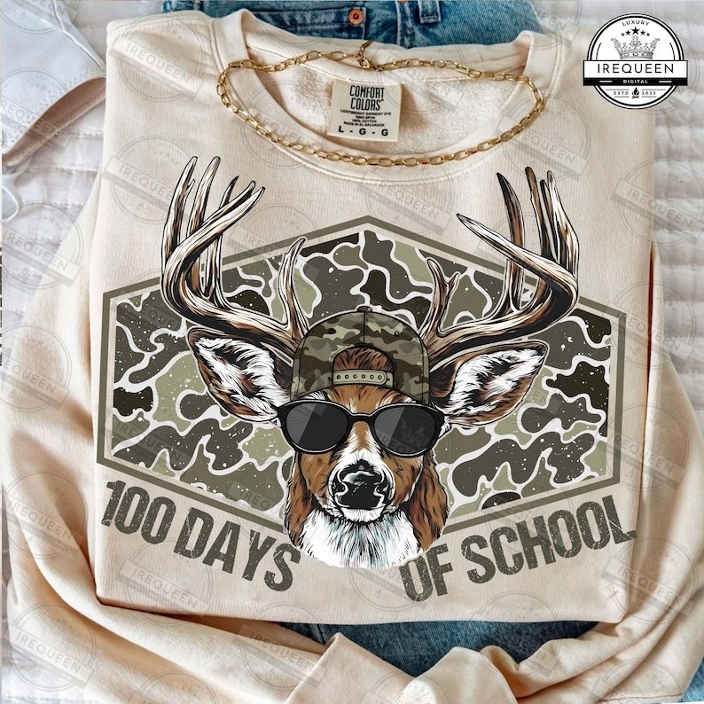 Puede incluir: Una sudadera beige con un gr&aacute;fico de un ciervo con gafas de sol y una gorra de camuflaje. El gr&aacute;fico est&aacute; sobre un fondo de camuflaje e incluye el texto "100 Days of School."