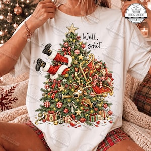 Puede incluir: Una camiseta blanca con un gráfico de un árbol de Navidad con las piernas de Santa Claus sobresaliendo por arriba, una cara de reno entre las ramas y un trineo rojo. El texto "Well, shit..." está impreso sobre el árbol.