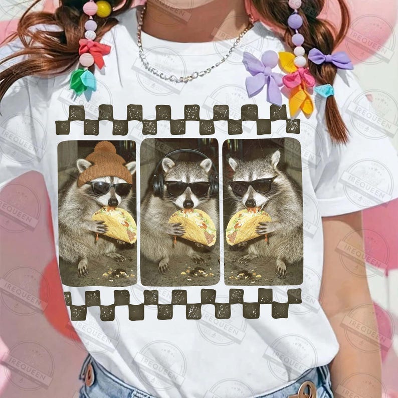 May include: White t-shirt with a graphic of three raccoons wearing sunglasses, each eating a taco. The raccoons are framed within a black and brown checkered border.