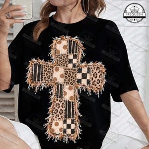 May include: A black short-sleeve t-shirt featuring a large, central cross graphic. The cross is composed of various patchwork squares with leopard print, polka dot, and checkered patterns, all outlined with a frayed, textured fringe edge.